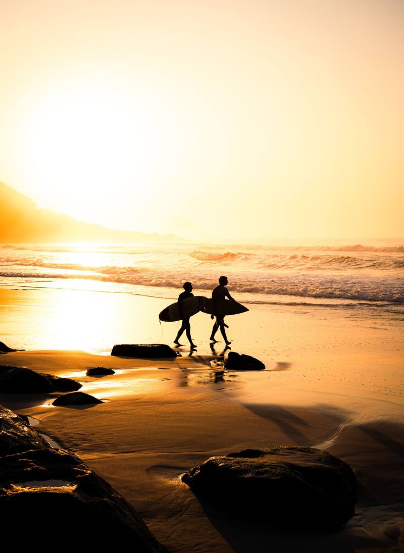 Deux surfeurs marchant sur la plage au coucher du soleil