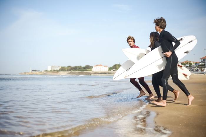 Trois surfeurs courant vers l'eau avec leurs planches