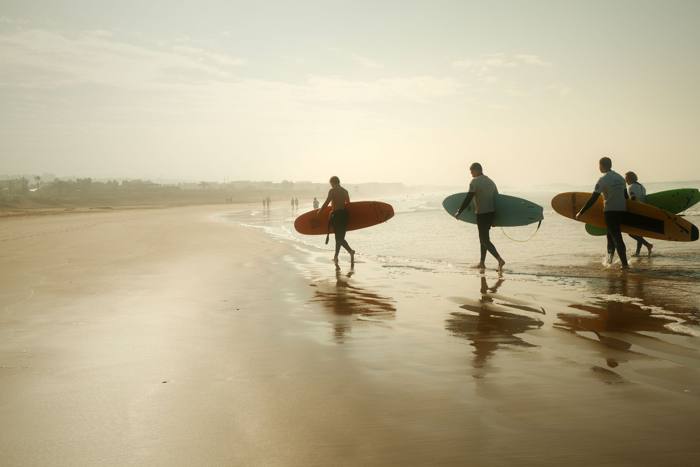 Surfeurs marchant sur une plage brumeuse au lever du soleil