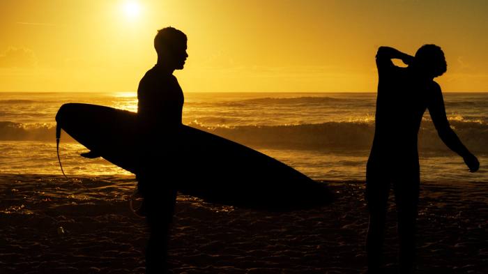Surfeurs en silhouette sur la plage à l'heure dorée